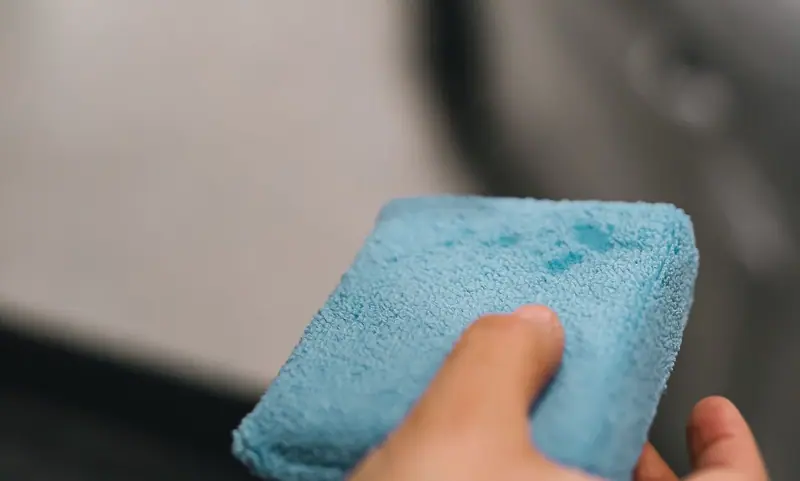 Hand holding a blue applicator pad over car paint