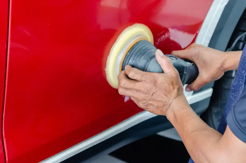 Polisher with a yellow pad correcting a red car door