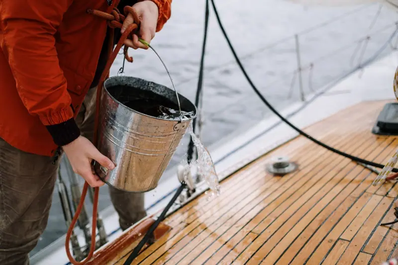 Hands with a bucket and hose washing a boat deck