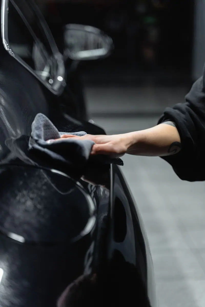 Gloved hand wiping a black fender with a microfiber towel