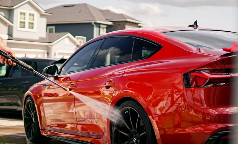 Red car being rinsed in a driveway in front of a house