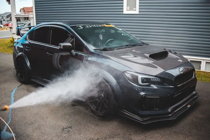 Dark car being rinsed with a spray wand in a driveway