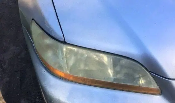 Yellowed, hazy headlight lens on a silver car before restoration